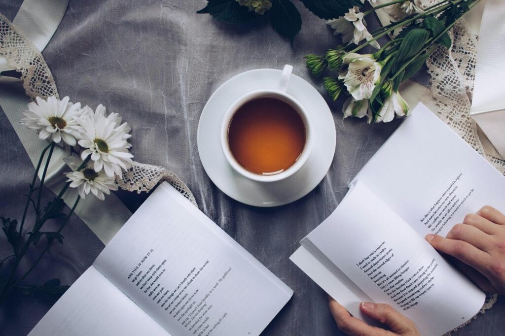 A person engrossed in reading a book, with another book and a cup of tea resting nearby.