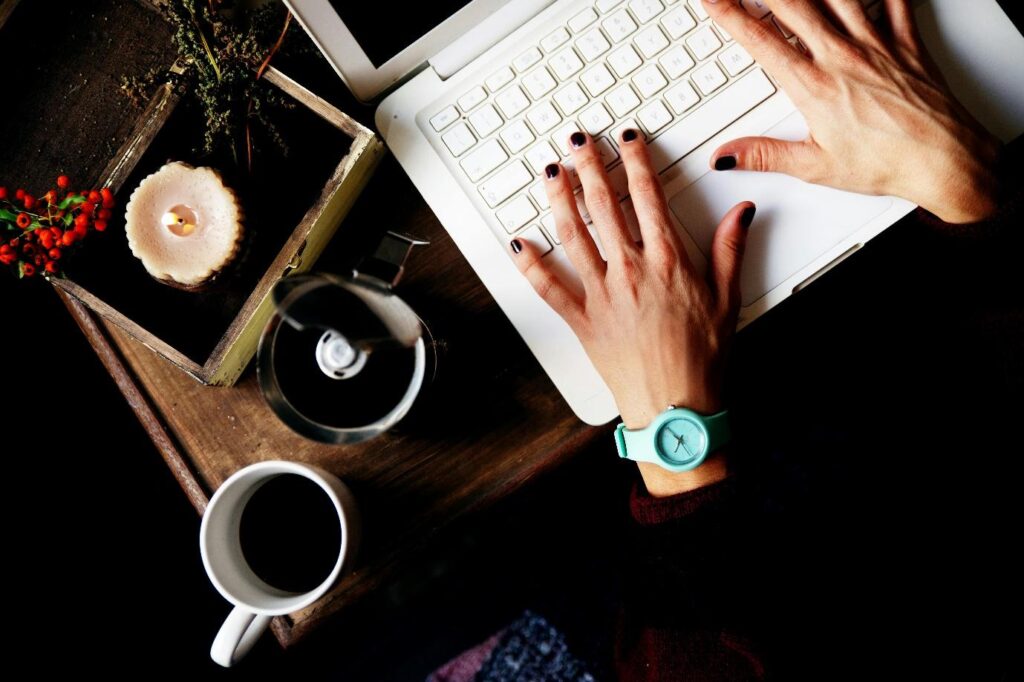 a girl working on her laptop and finding average book length with a cup of black tea and scented candle placed nearby.