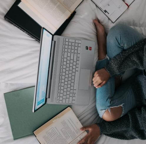  Someone sits cross-legged on a bed with a laptop