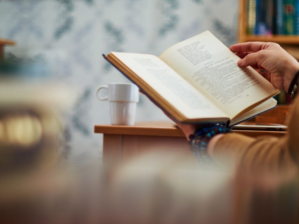 a woman enjoying her book with a cup of tea placed on her table