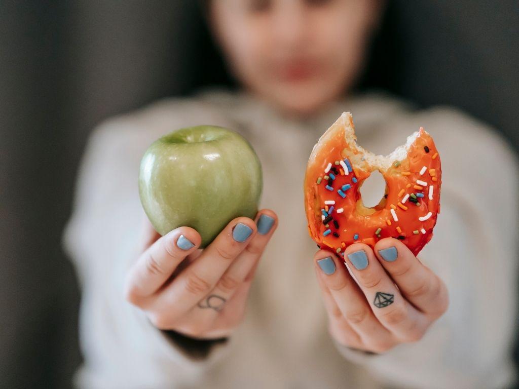 a girl holding an apple and a donut for comparison