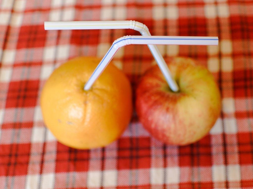 an apple and orange placed side by side with straws on them showing comparison