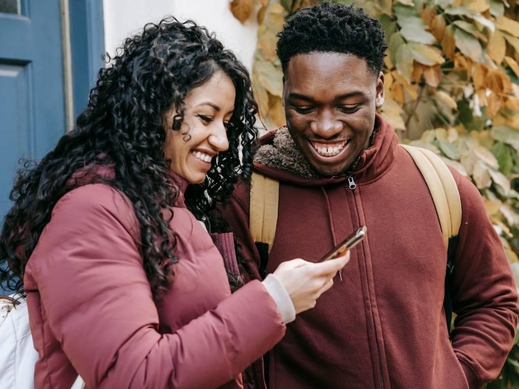 A happy couple smiling while looking at their phone, sharing a joyful moment.