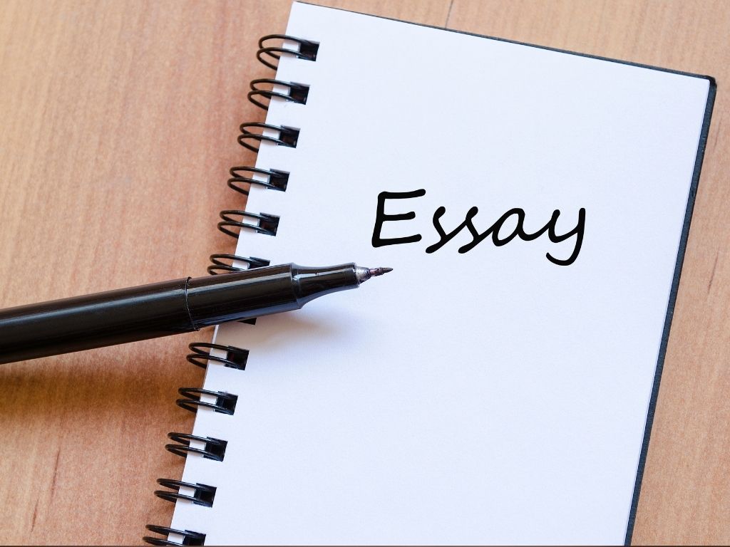 the word essay written on a notebook with a black pen placed on top