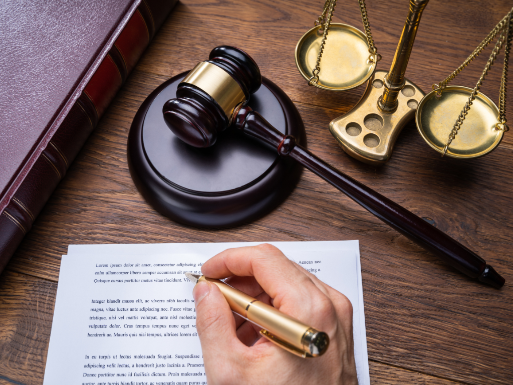 A person reading from a book, with a balance scale and a judge's gavel placed nearby, symbolizing justice and law.