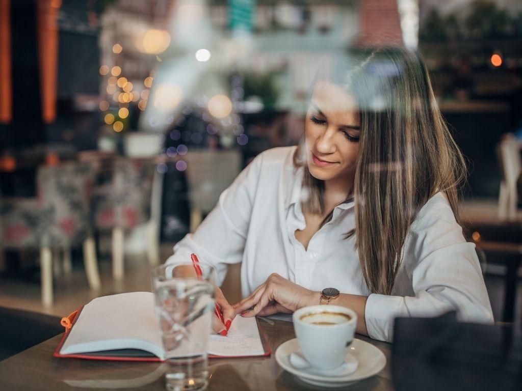 A girl writing in her notebook while enjoying a cup of coffee in a cozy café.