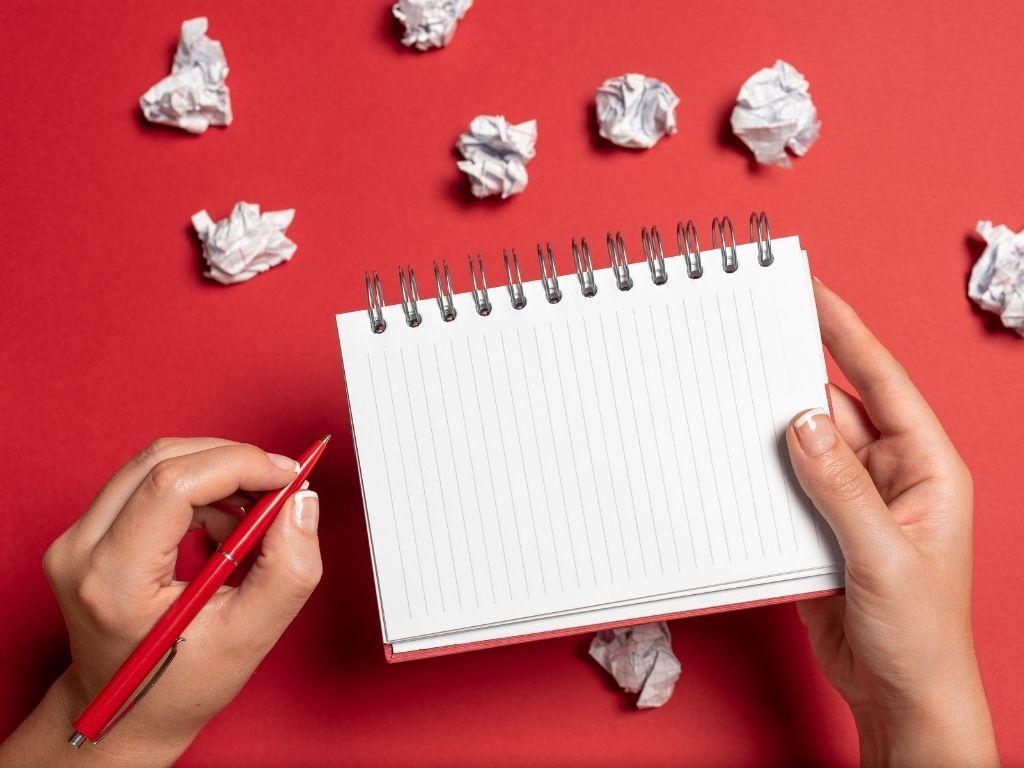 a girl holding a red pen and ready to write something on her Notebook