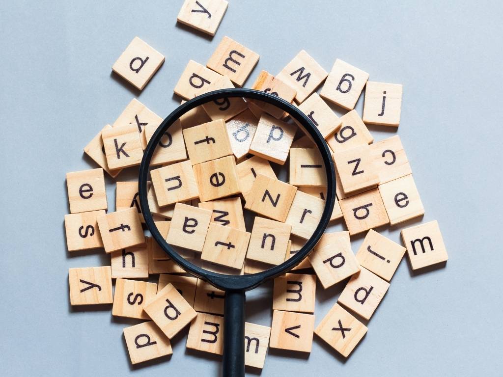 A magnifying glass placed over Scrabble tiles, highlighting the letters.