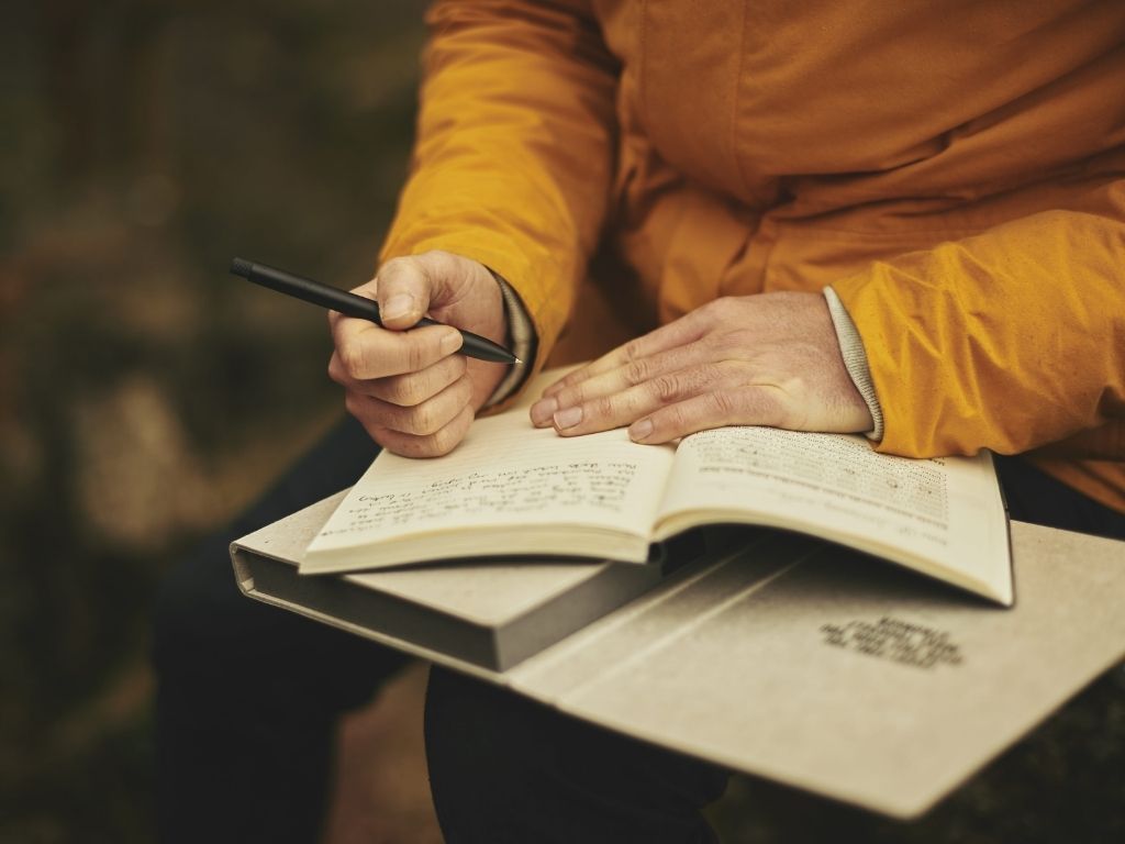 A boy writing something about how to use Transition Words to Start a Paragraph in his book with a black pen