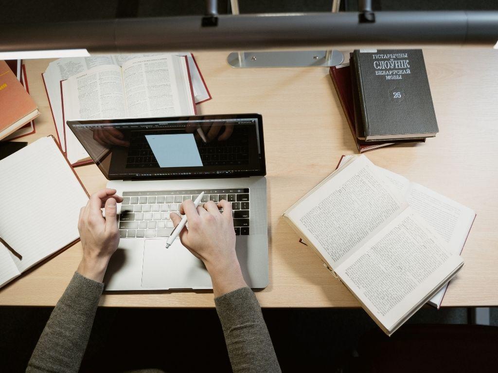 a person working on a laptop with books placed on the table 