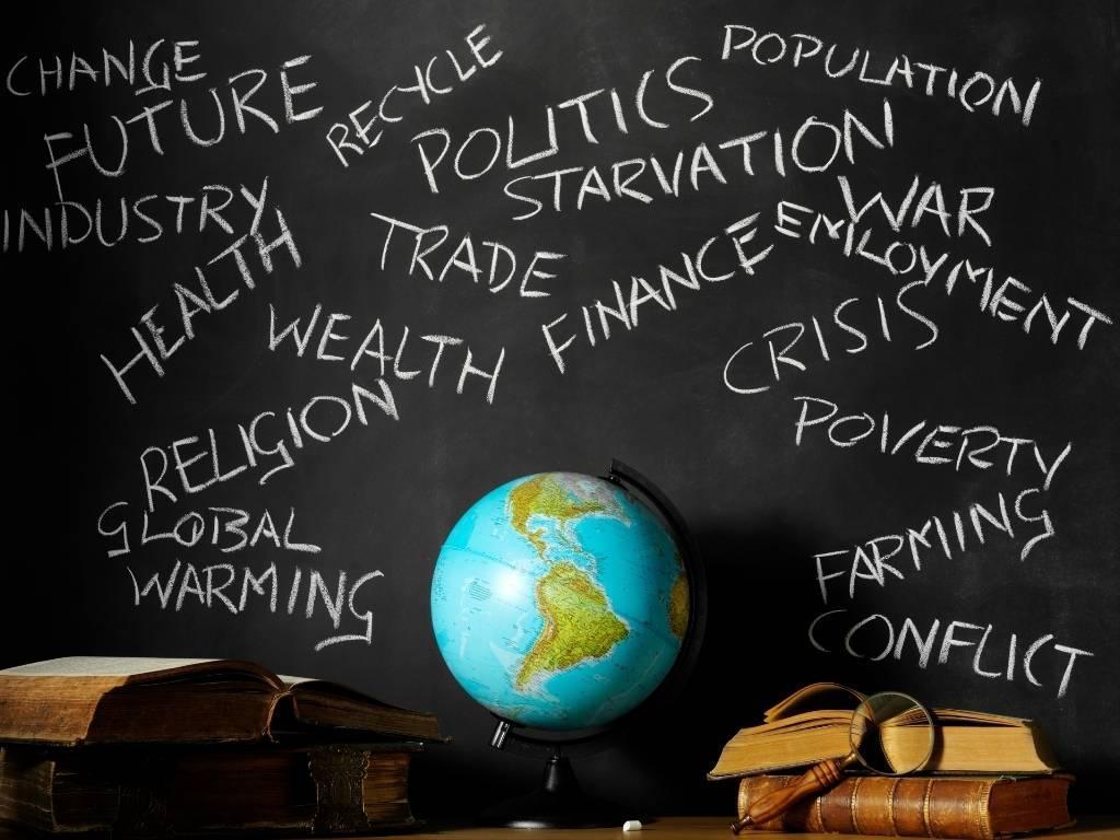 a globe placed in front on a black board with several words written on it that show how the world is being affected