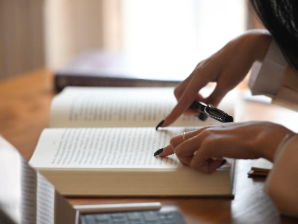 a girl pointing on her book while her laptop placed nearby