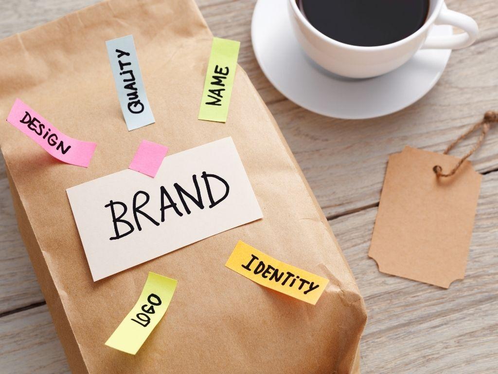 An image of a package on a table adorned with various tags, each labeled with terms like "Brand," "Identity," "Logo," "Design," and "Name." A cup of coffee is placed nearby, adding a cozy and creative ambiance to the workspace.