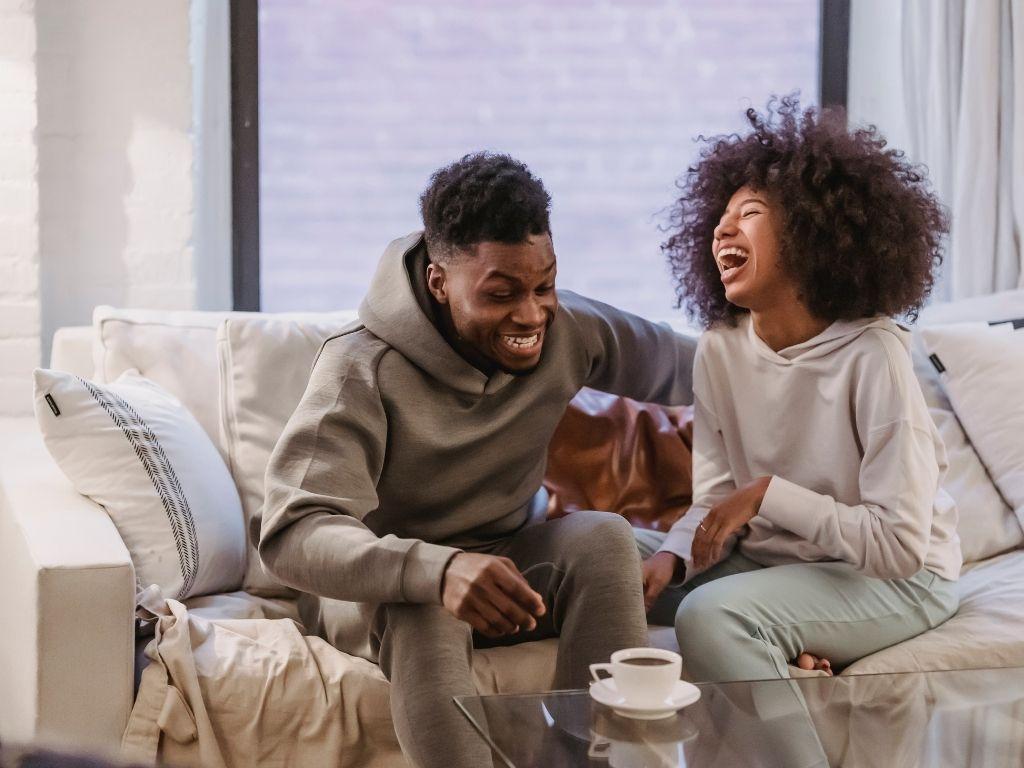 a couple laughing and enjoying their cup of coffee while sitting on a sofa