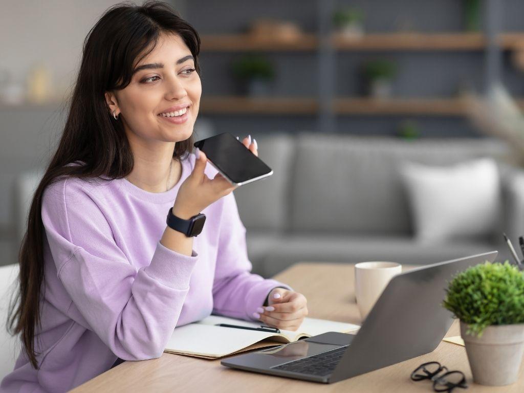 A girl engaged in a phone conversation, with a book and laptop placed in front of her on the table, creating a balanced scene of multitasking and focus