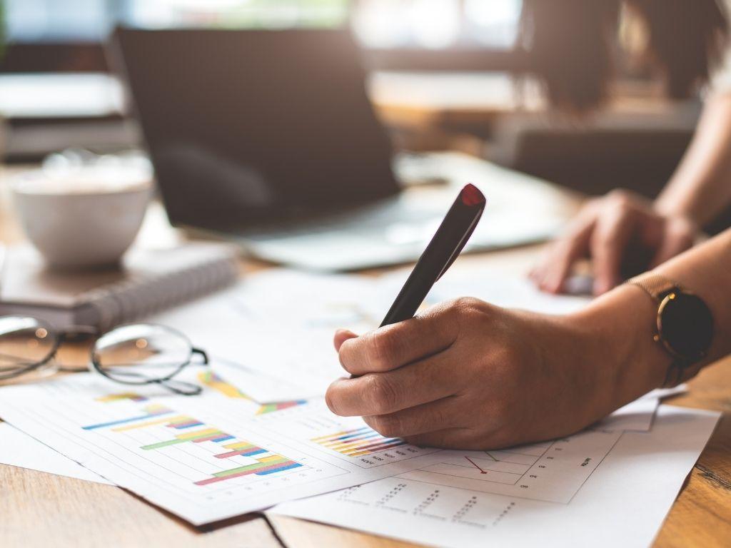 A person writing notes with paperwork spread out across the table about how to write an executive summary.