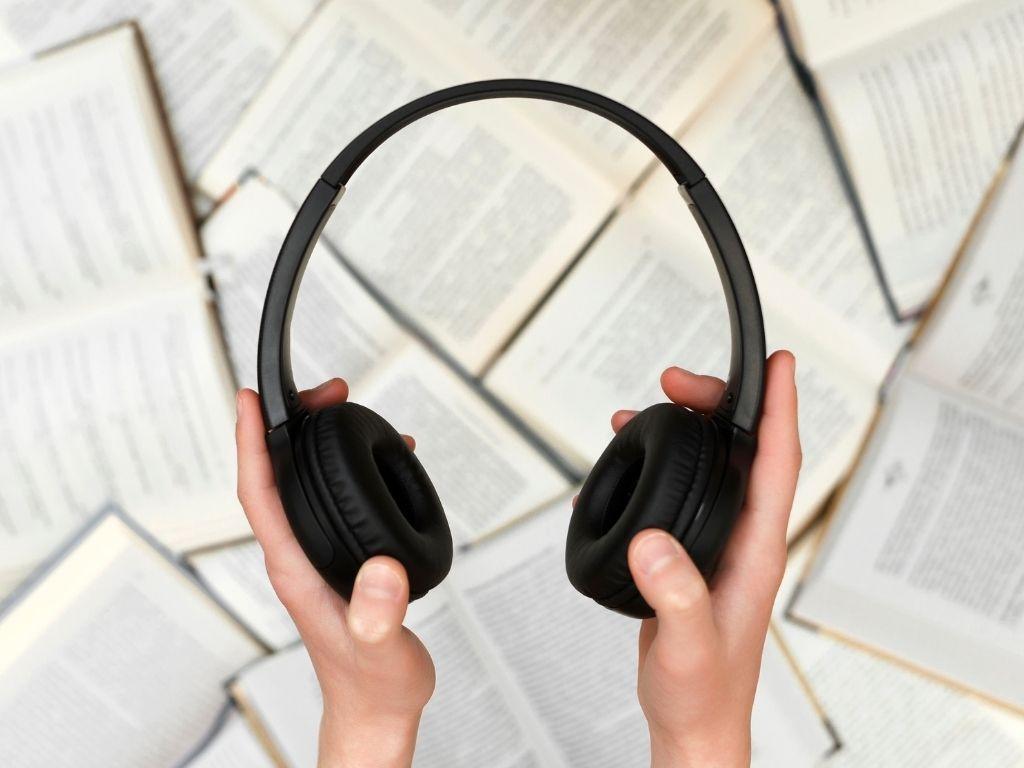 a man holding a headphone over some books placed beneath