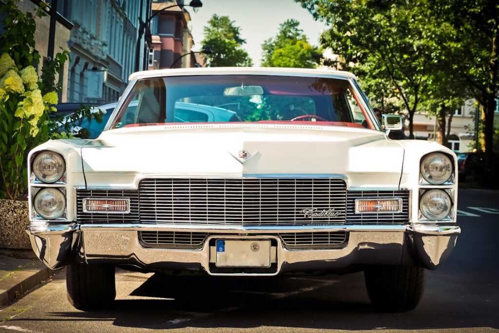 Free Front view of a classic white Cadillac parked on a sunny street with trees. Stock Photo