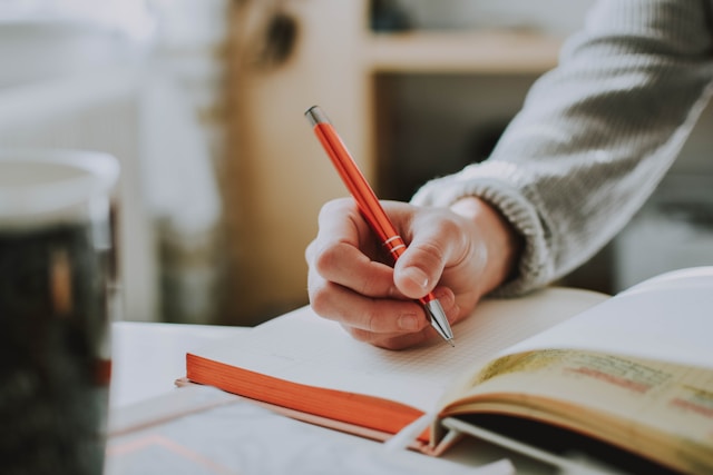 A person writing in a book with a red pen