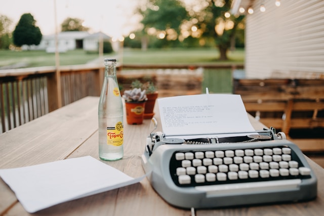 A Typewriter and a drinks bottle on a table outside 