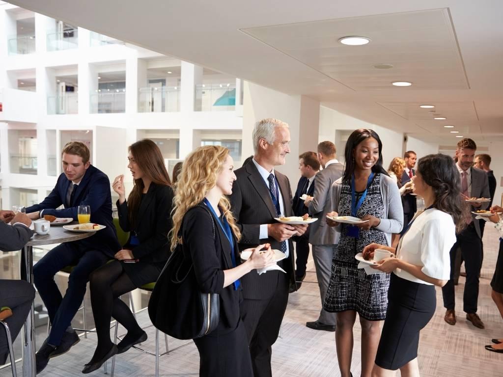 A group of professionals engaged in a lively discussion in a modern office café, surrounded by coffee cups and notepads.