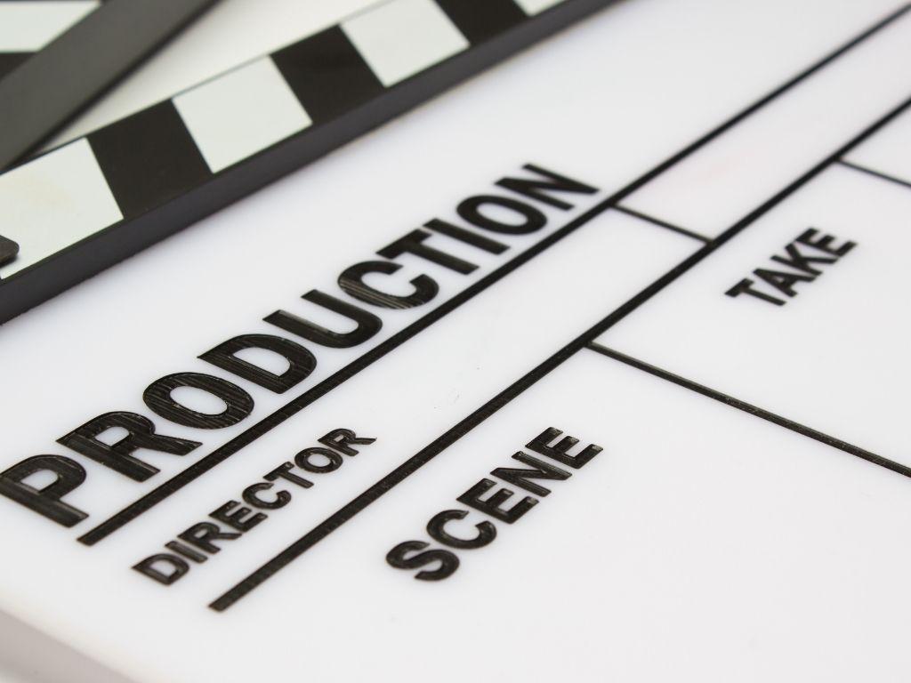 A "Scene Take" clapperboard placed on a surface, with the word "Production" highlighted at the top.