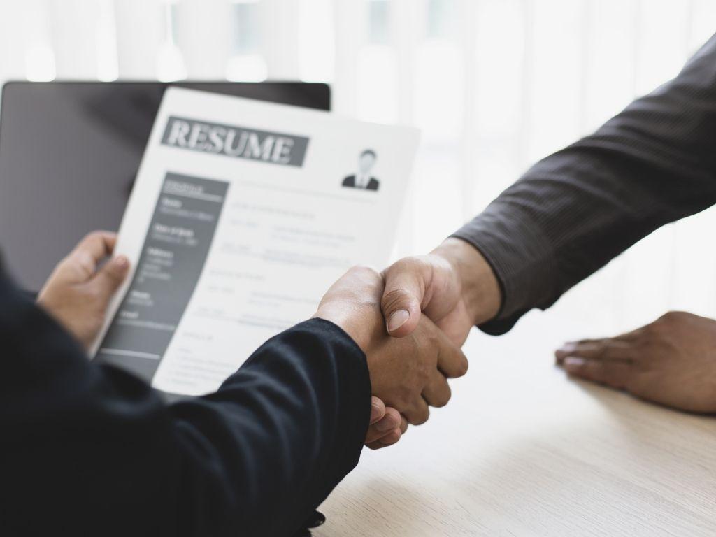 two men shaking their hands while one is holding a resume