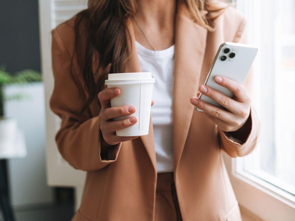 a girl holding a cup of coffee and a phone in other hand