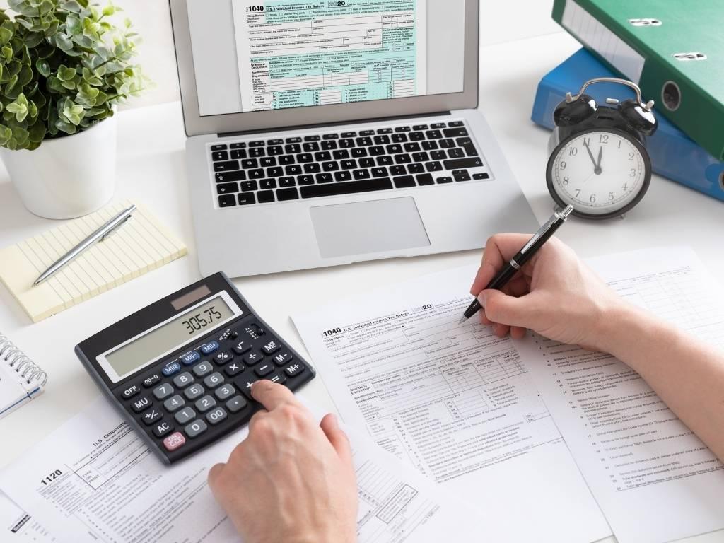 A man working on his laptop, calculating figures on a calculator, and filling out a form simultaneously.