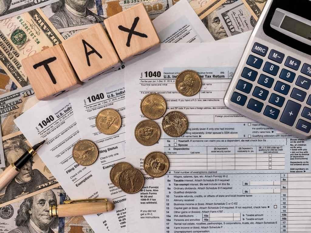 calculator, tax, coins, a pen and cash placed on a table showcasing bookkeeping work.