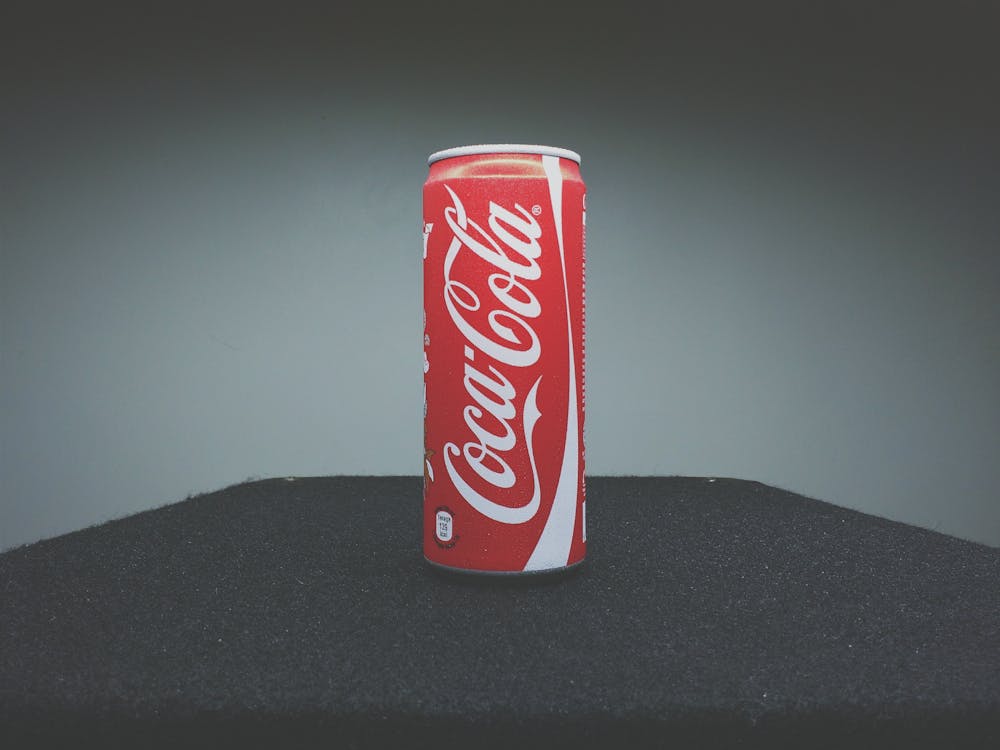 Free A classic Coca-Cola can showcased on a dark surface with minimal lighting. Stock Photo