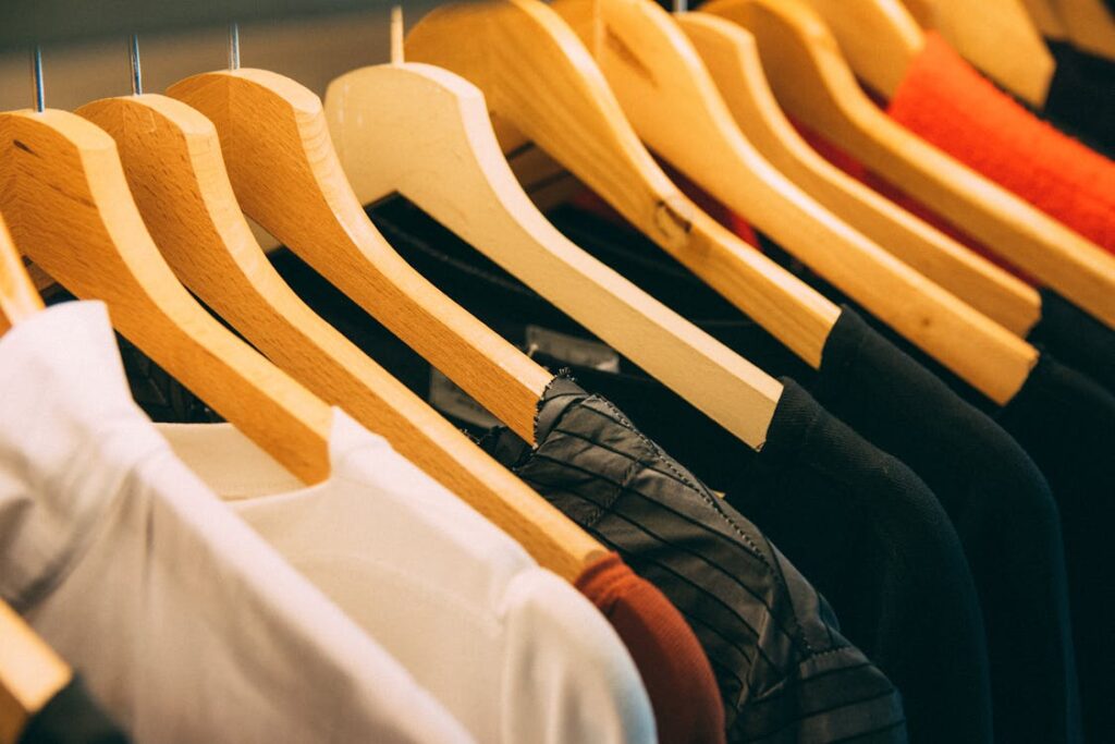 Free A close-up view of a row of clothes on wooden hangers, showcasing various fabrics and colors in a wardrobe setting. Stock Photo