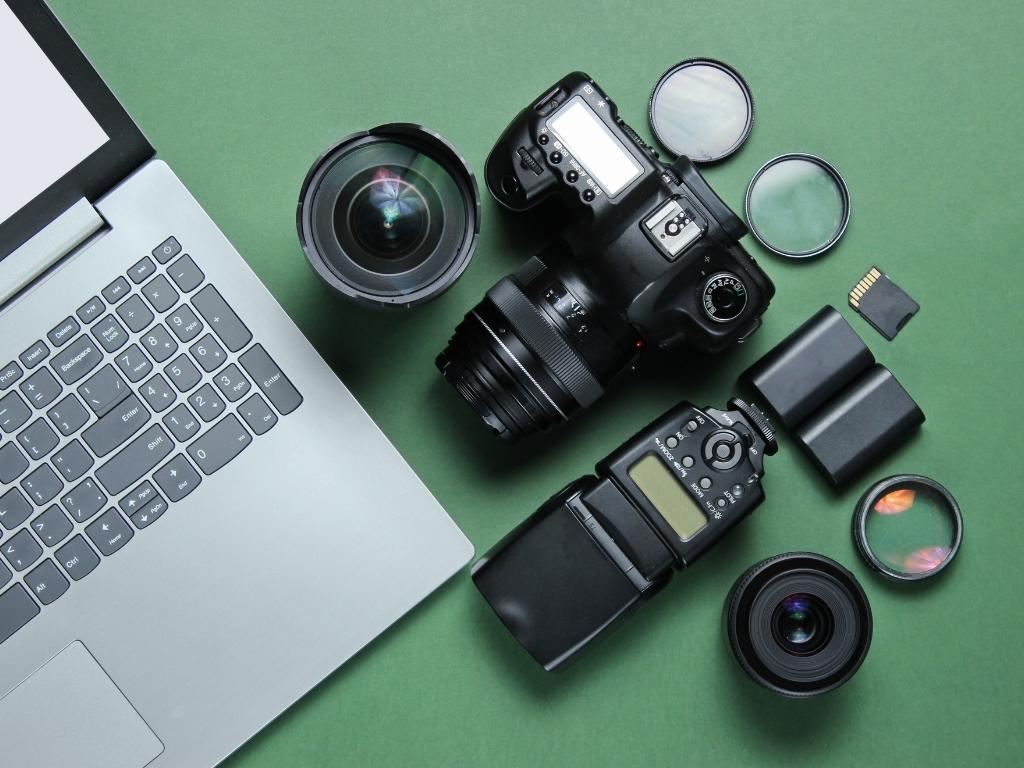 a DSLR camera placed on a desk with its accessories alongside a laptop.