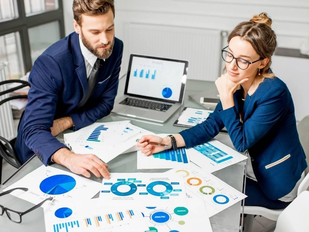 Two people engaged in a discussion about business growth, analyzing multiple sheets spread across the table.