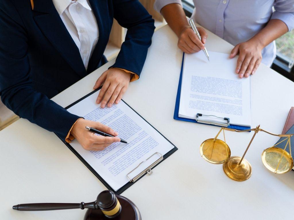 Two people collaborating on a report, with a balance scale and a judge's gavel placed on the table.