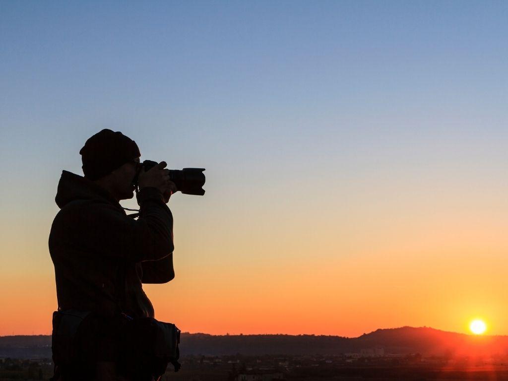 a man taking a photo of a beautiful sunset in his dslr.